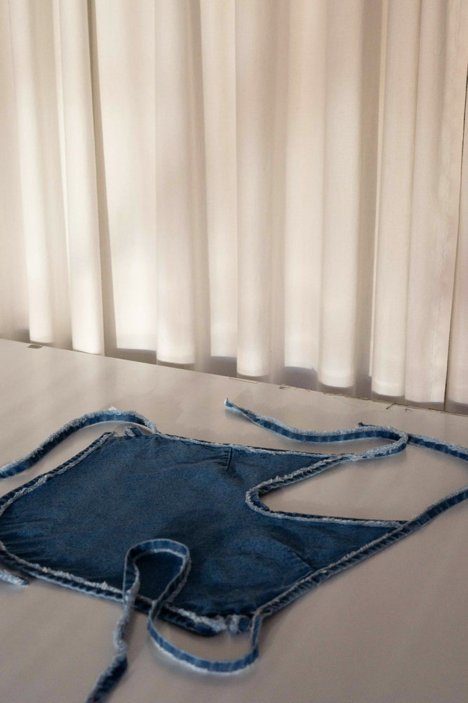 Halter denim top with rounded hem and adjustable waist with lacing in back. This white denim halter top has been crafted with contrast stitching in a toasted ocre color. 