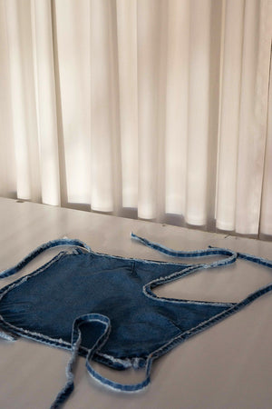 Halter denim top with rounded hem and adjustable waist with lacing in back. This white denim halter top has been crafted with contrast stitching in a toasted ocre color. 
